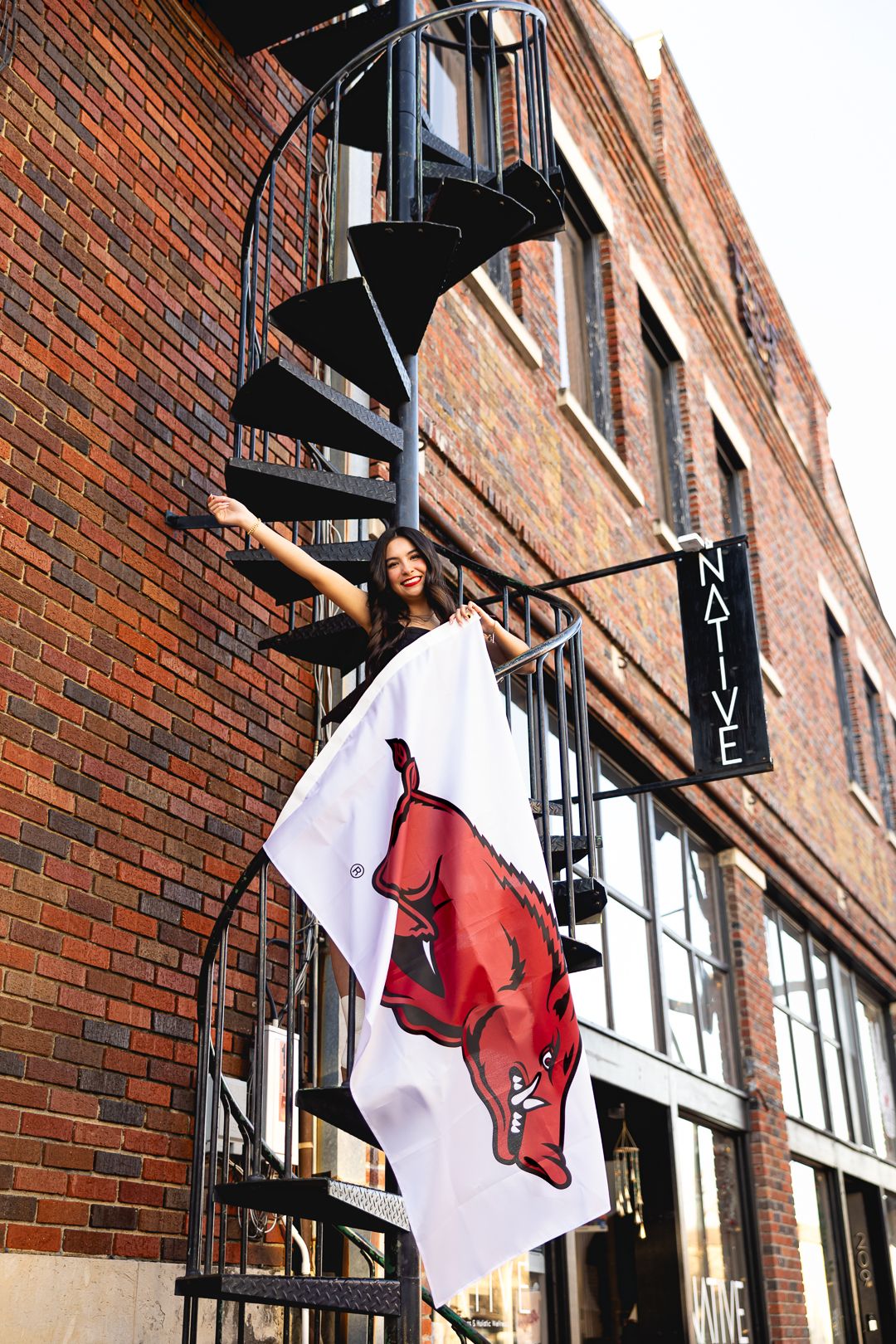 A red cardinal mascot flag hangs from a brick building's exterior with black spiral stairs visible in the background.