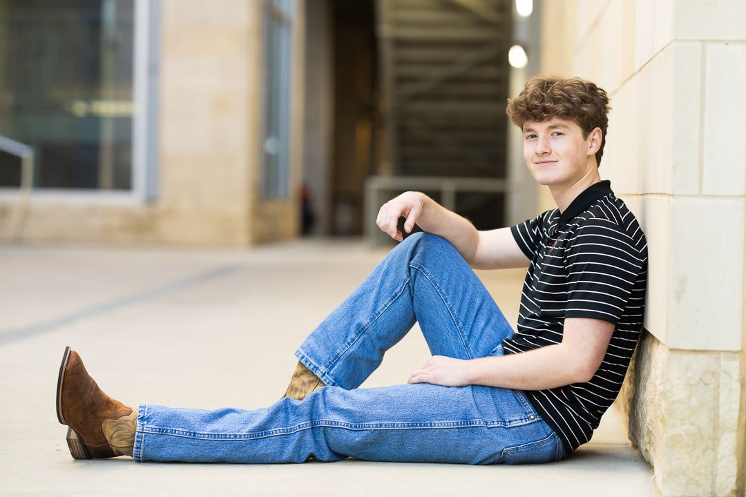 Person in striped shirt and jeans relaxing on wooden floor while looking at camera.