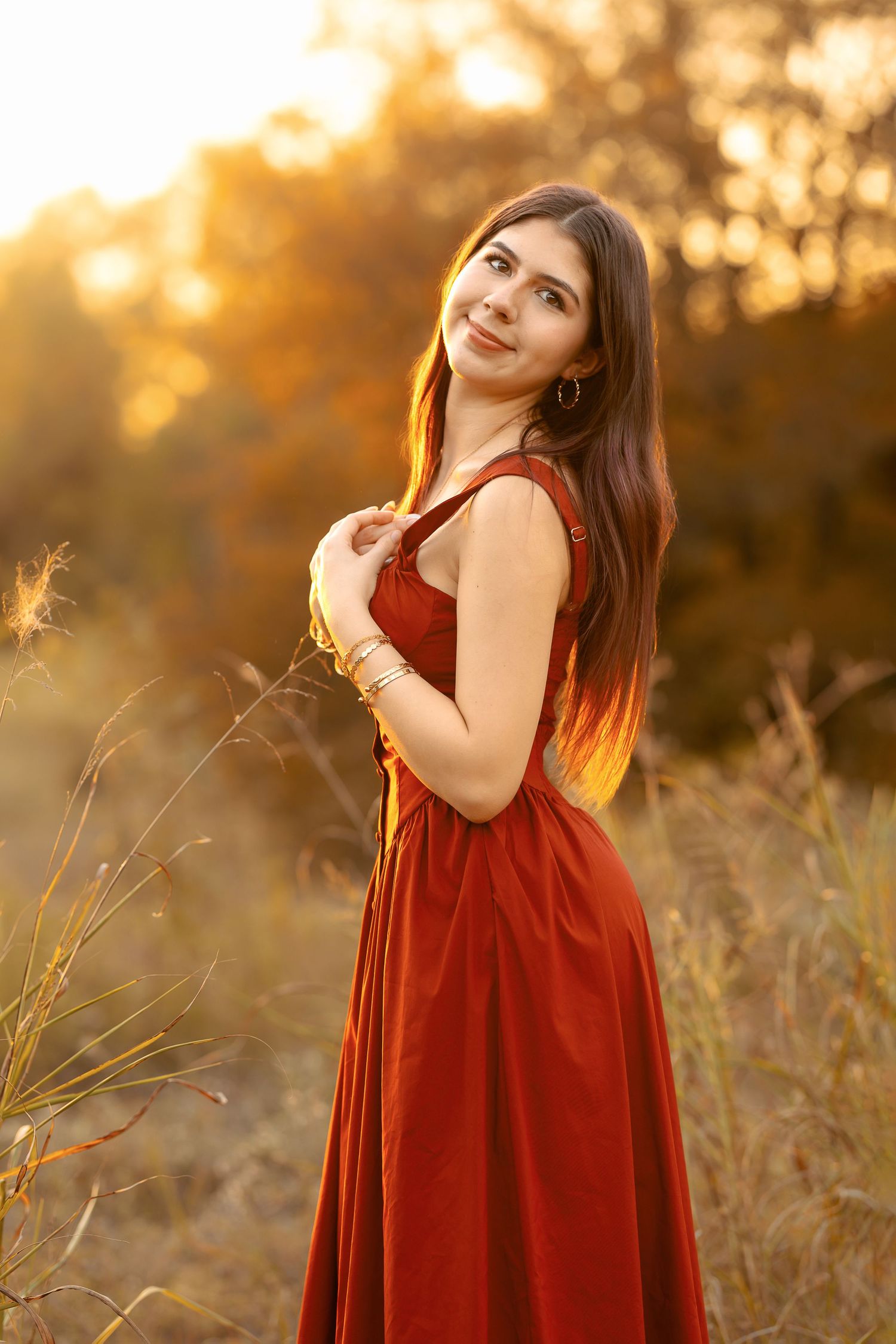 A person in a flowing red velvet dress poses gracefully in a golden sunlit field during sunset.
