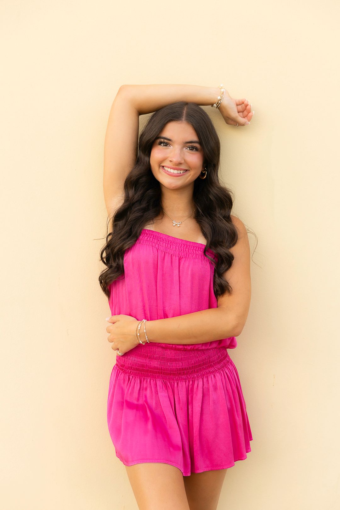 Portrait series against cream wall wearing vibrant pink top with ruffled details.