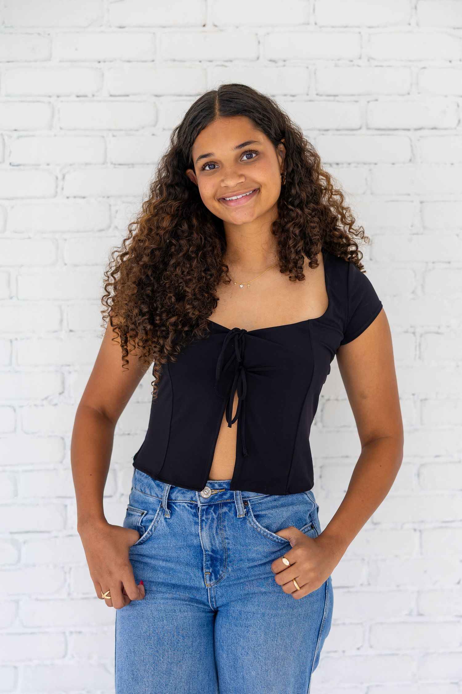 A series of casual fashion poses against a white brick wall wearing a navy top and blue jeans.
