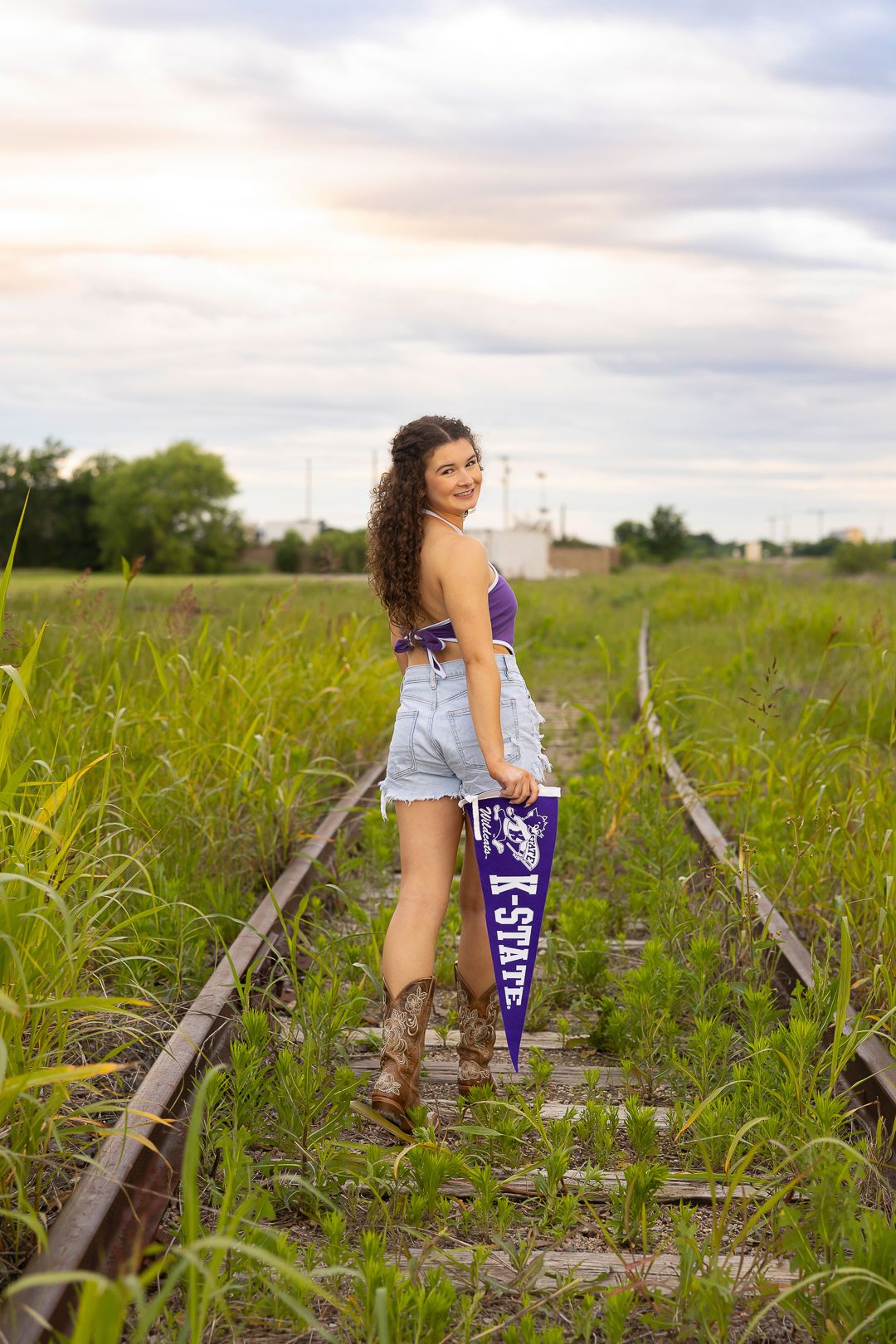 Purple school pennant displayed along abandoned railroad tracks in rural field.