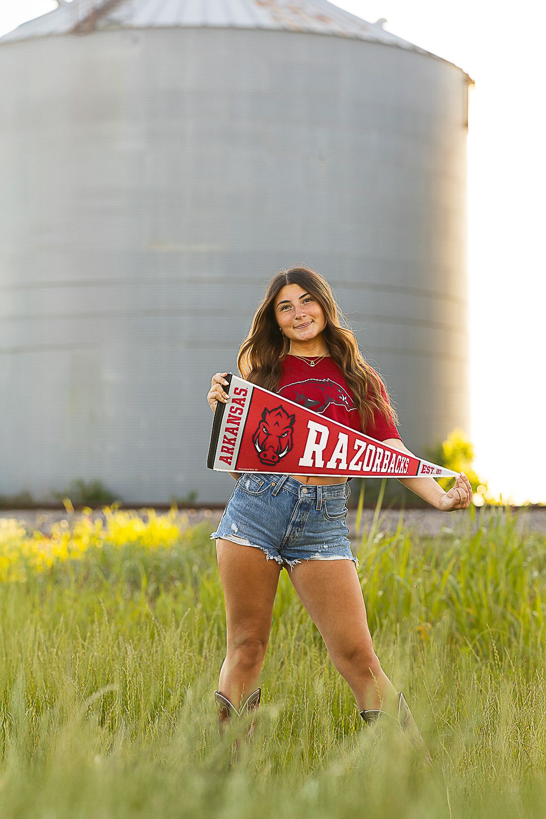 Red sports pennant displayed in grassy field with grain silos in background.