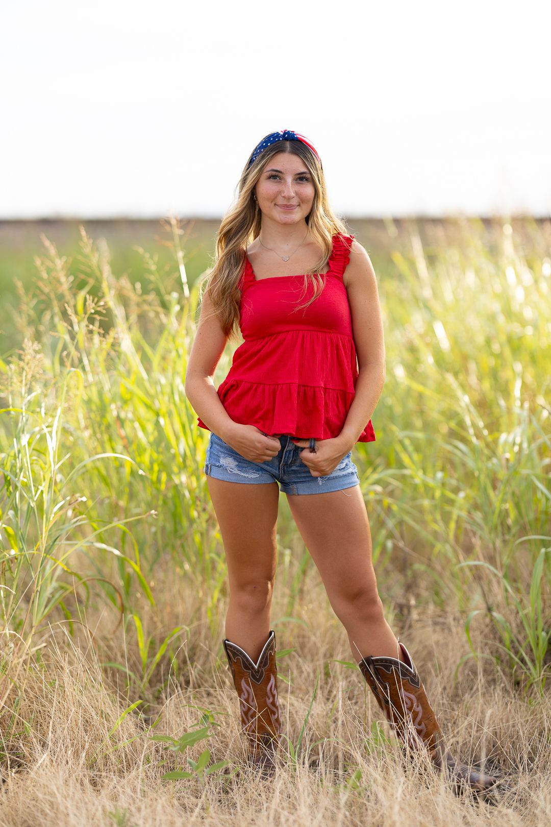 Red summer top and cowboy boots styled in golden field during outdoor country photoshoot.