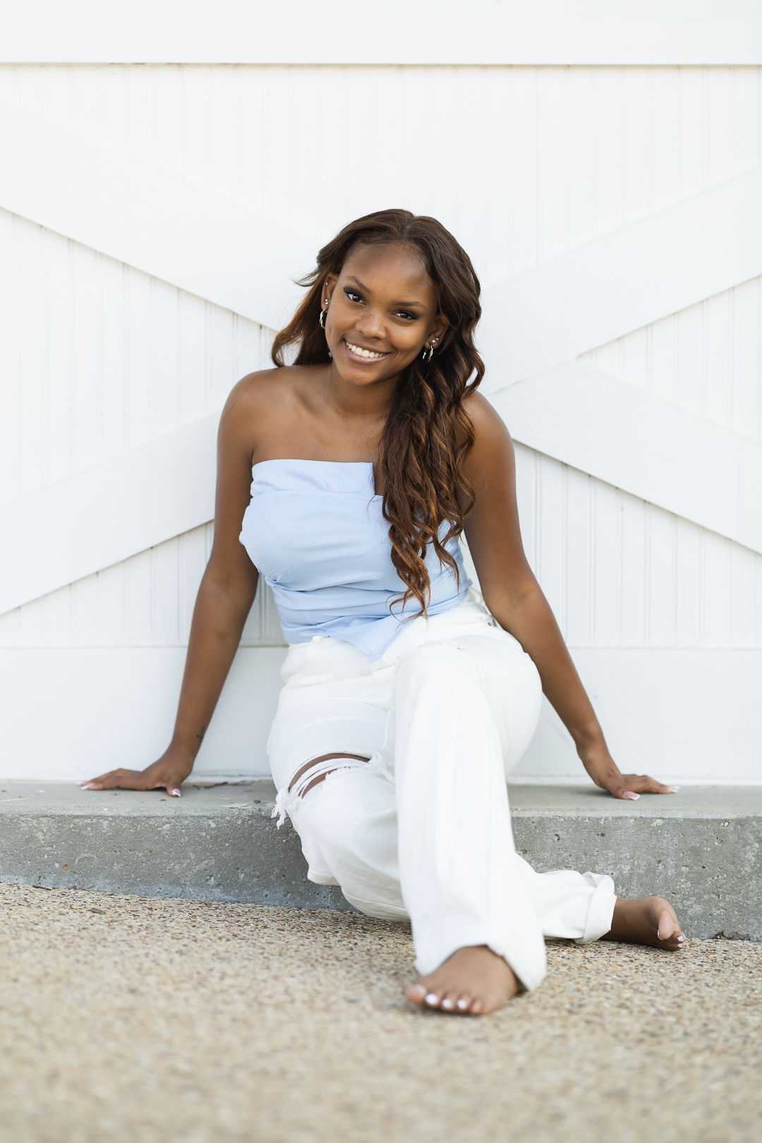 A person in a white outfit sits on the ground against a white wall in a relaxed pose.