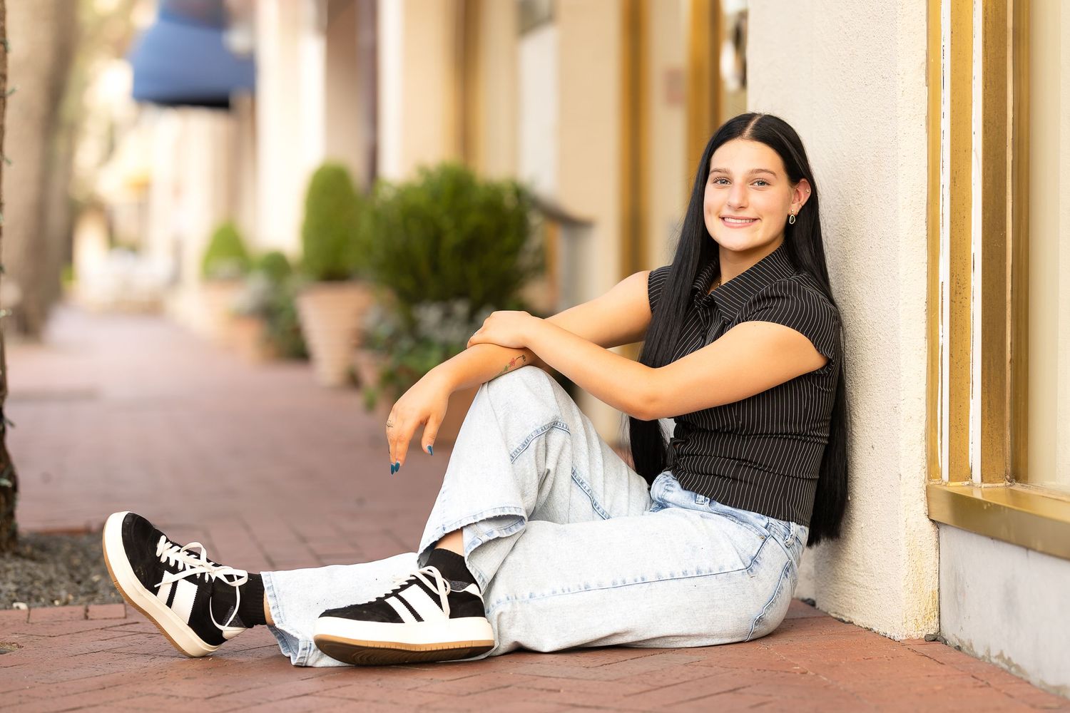 Person in casual attire relaxes on ground wearing black and white sneakers against a light-colored wall.