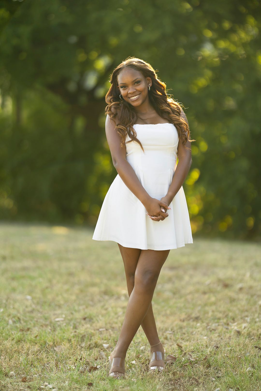 A person in a white dress twirls playfully on grass in golden sunlight.