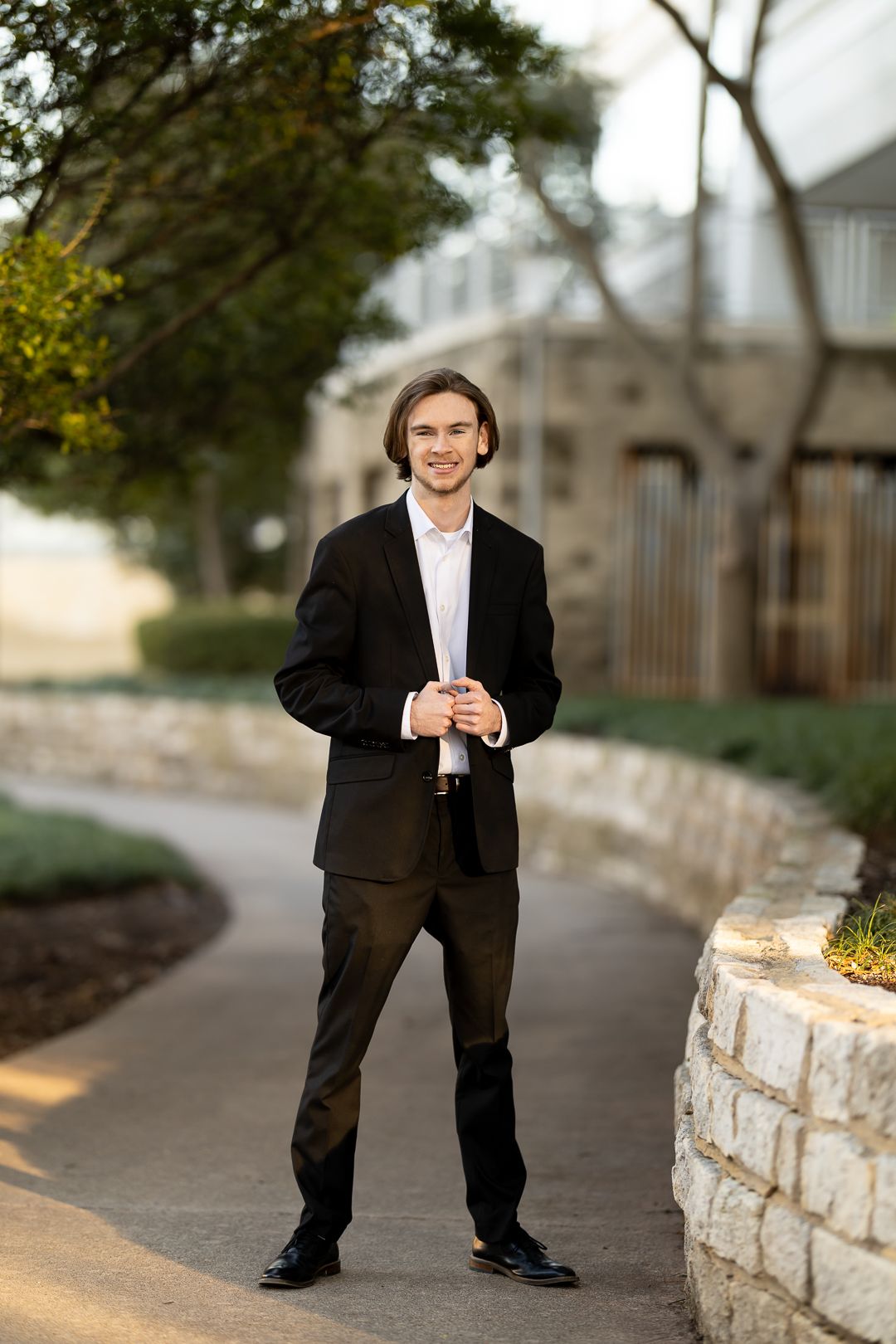 A series of outdoor portraits showing someone in a black suit standing against a stone wall in warm evening light.