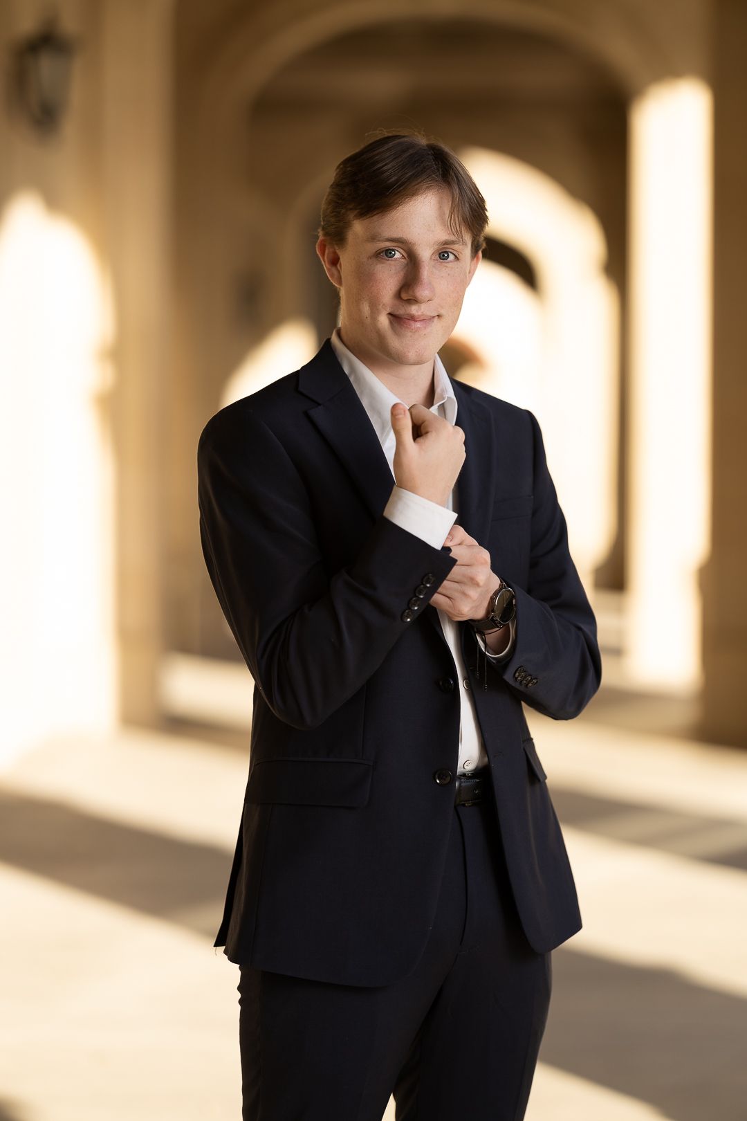 Professional portrait series showing a person in a dark business suit making thoughtful gestures in a sunlit hallway.