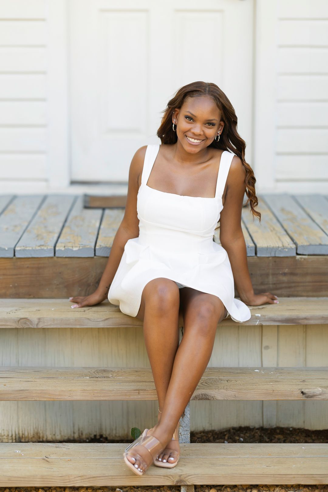 A person in a white dress sits on wooden porch steps.