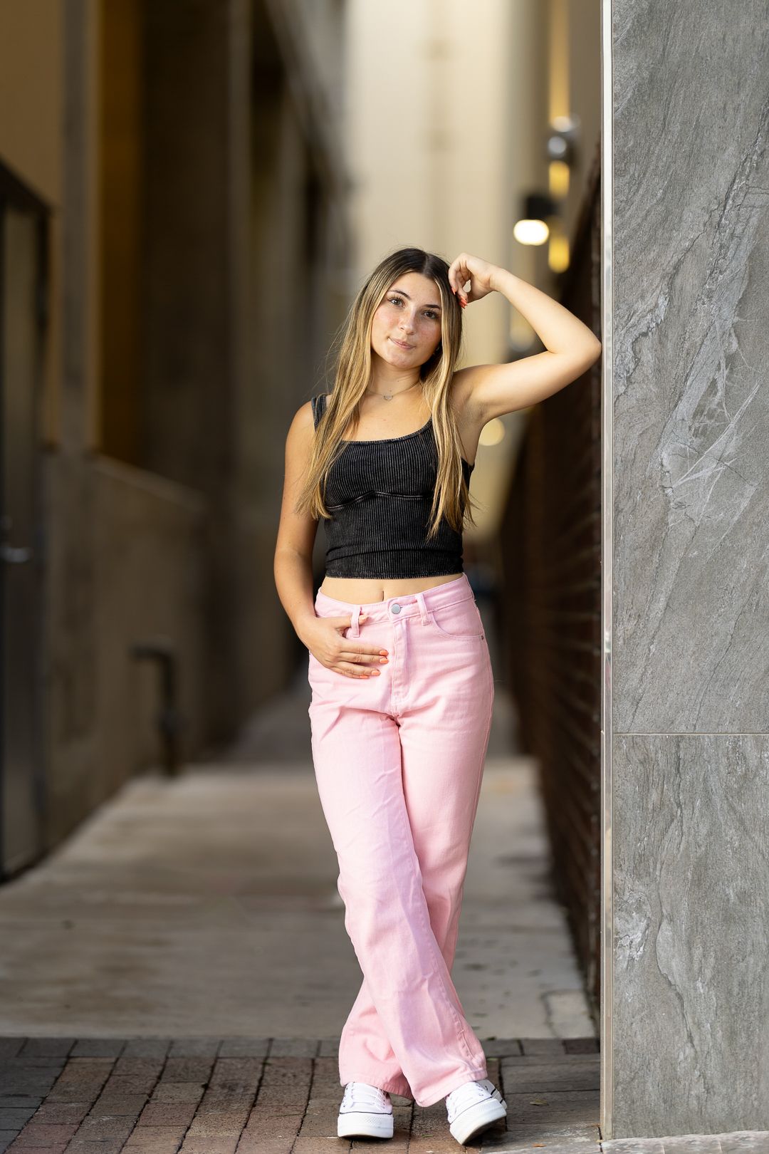Street style fashion pose featuring pink pants and black top in urban corridor setting.