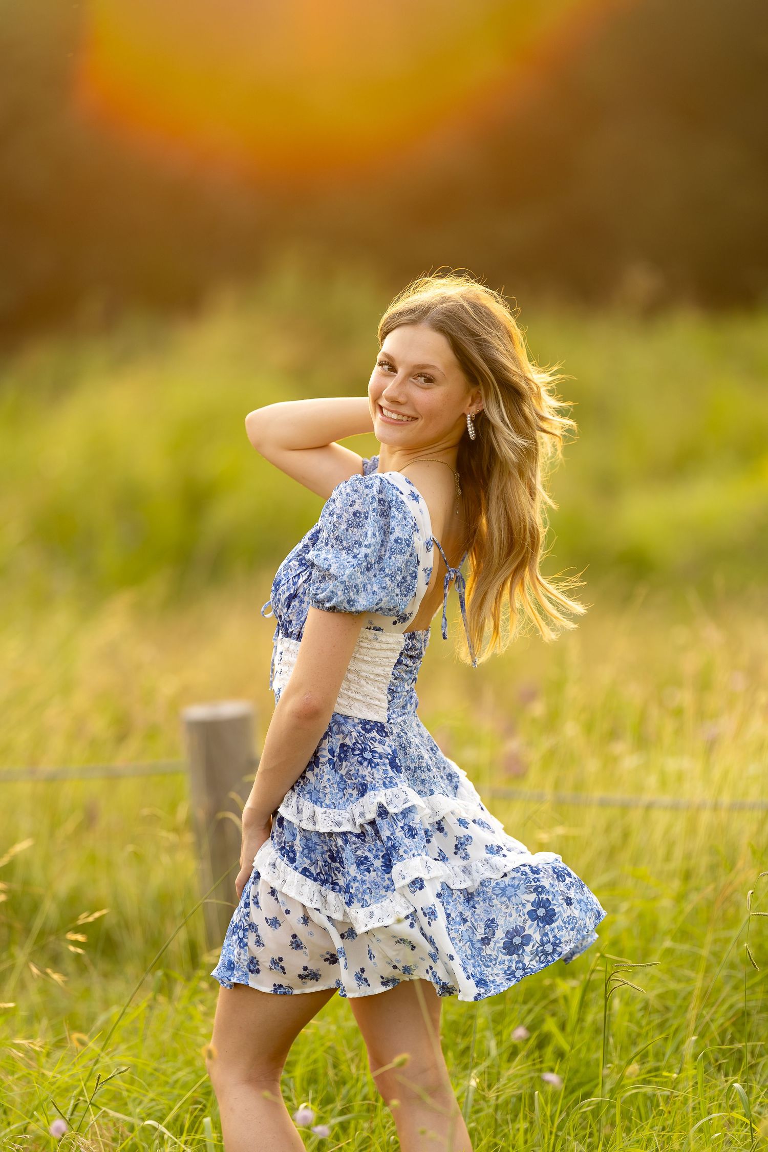 A person in a blue and white floral dress twirls in a sunlit meadow at golden hour.