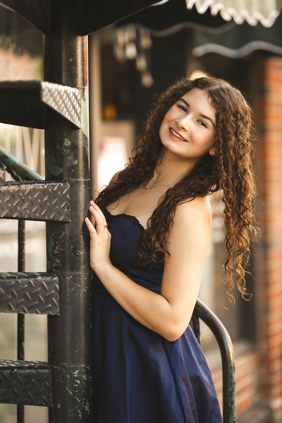 Urban fashion shoot featuring navy dress and curls against industrial metal backdrop.