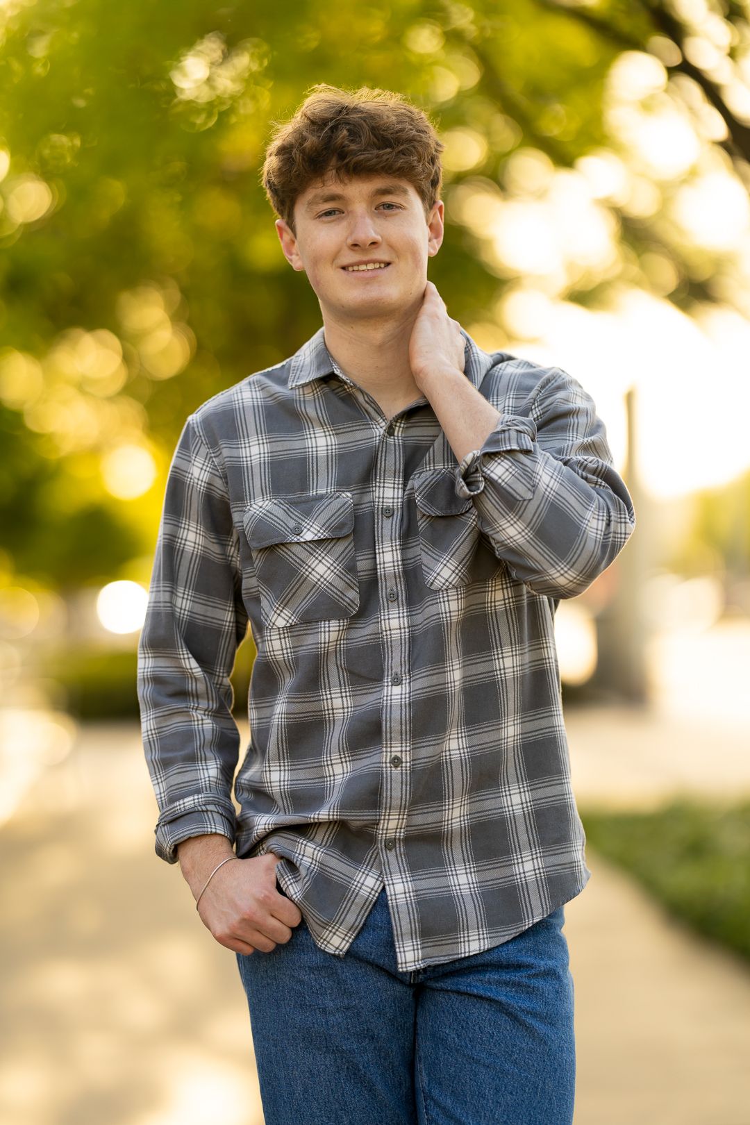 Casual portrait session featuring plaid shirt and jeans against natural outdoor backdrop.