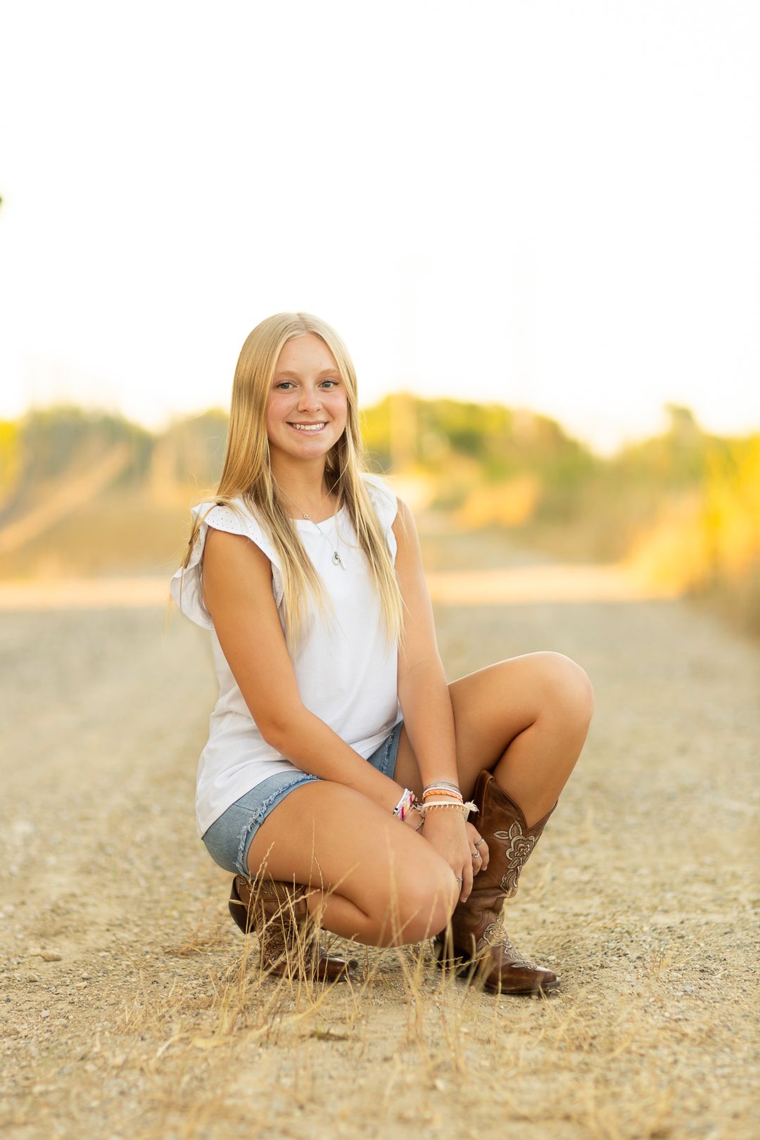 Portrait session at golden hour showing casual summer style with denim shorts and boots on dry grass.