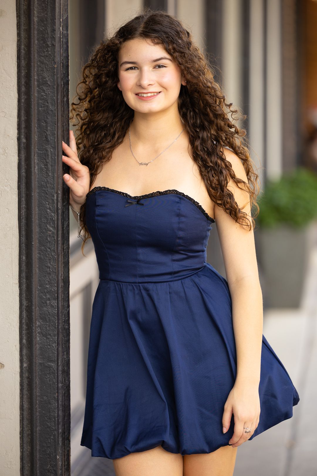 A person wearing a navy blue dress poses outdoors against a light-colored wall in a four-photo collage.
