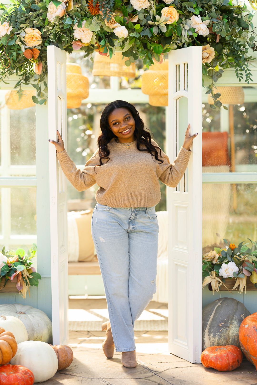 Casual fall portraits with pumpkins and floral arrangements in a bright greenhouse setting.
