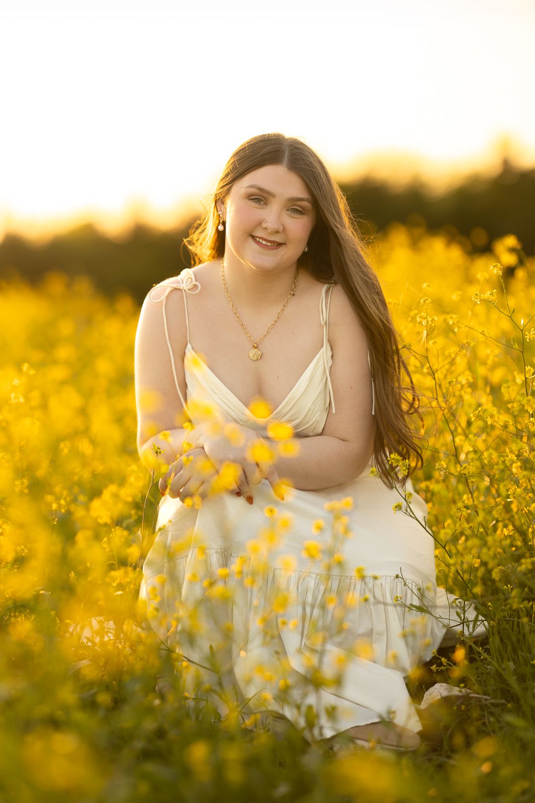 A person in a white dress sits among vibrant yellow wildflowers during golden hour sunset.