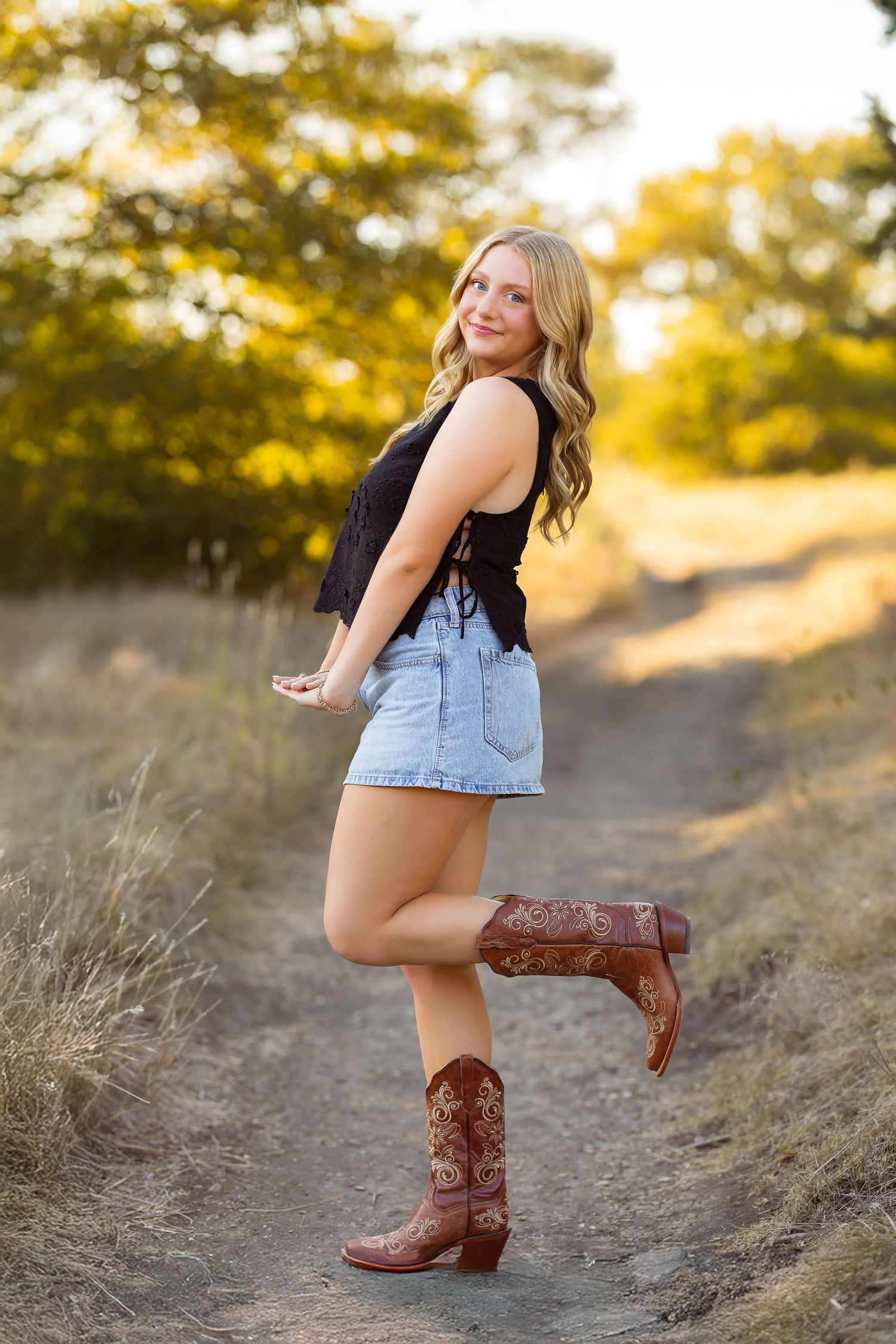 A person in denim and brown cowboy boots poses on a hillside during golden hour sunset.