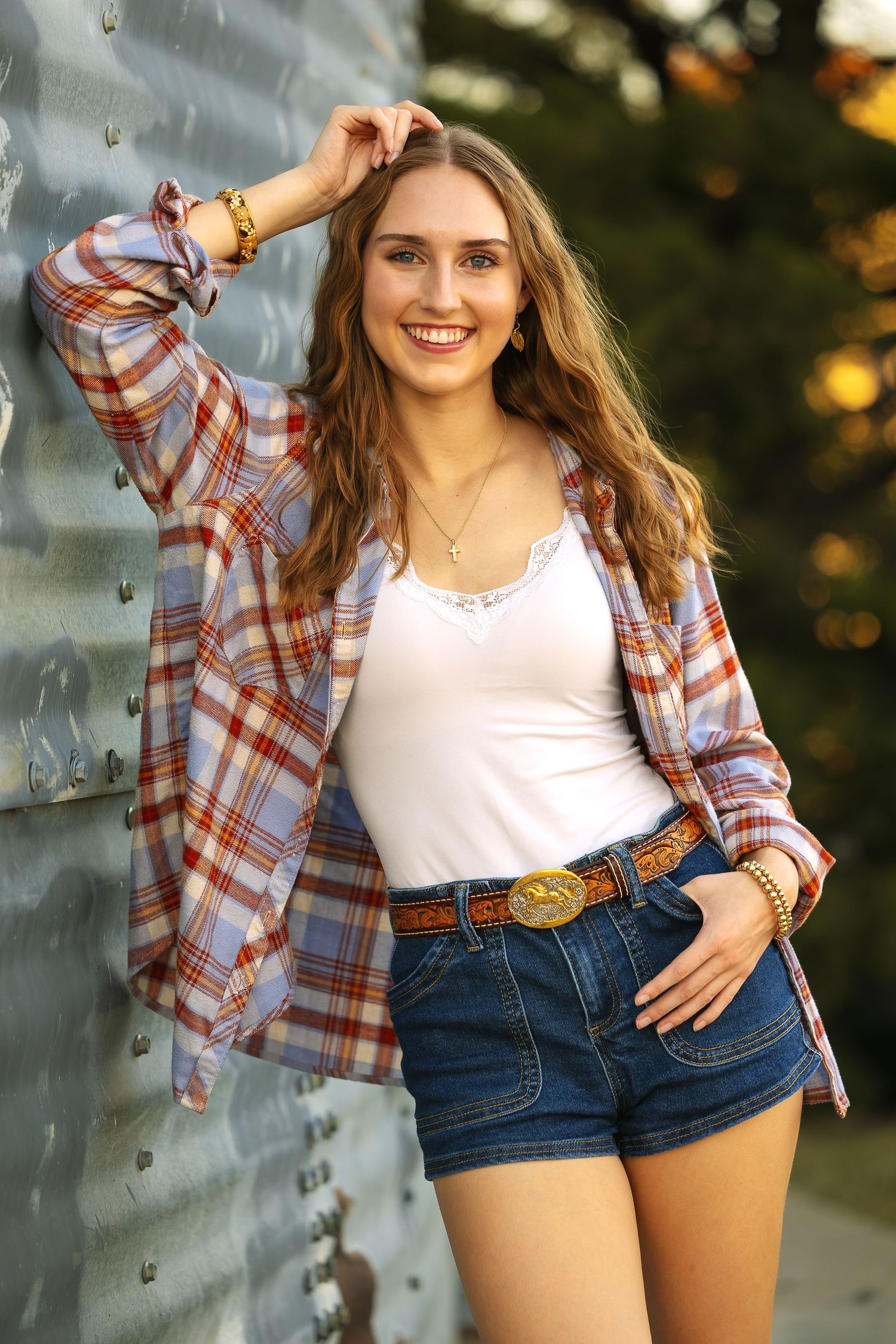 Casual summer outfit with plaid flannel shirt over white tank top paired with denim shorts and brown leather belt.