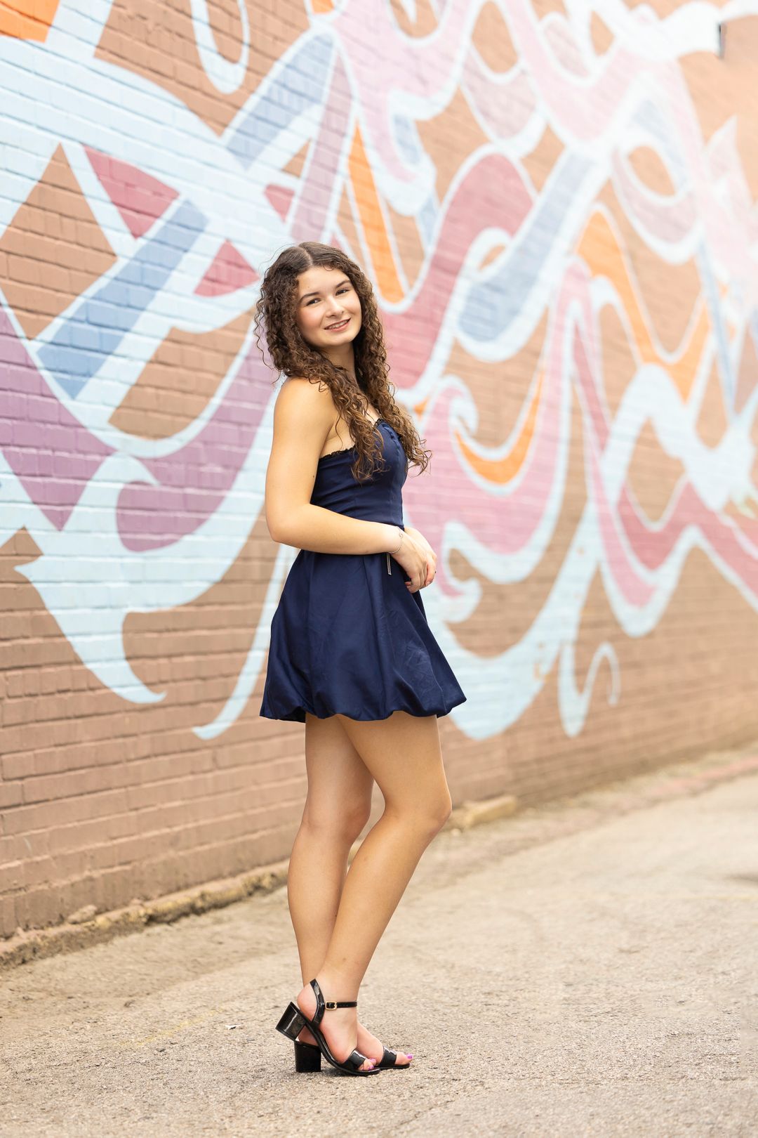 Fashion portrait against colorful graffiti wall in navy blue dress and heels.
