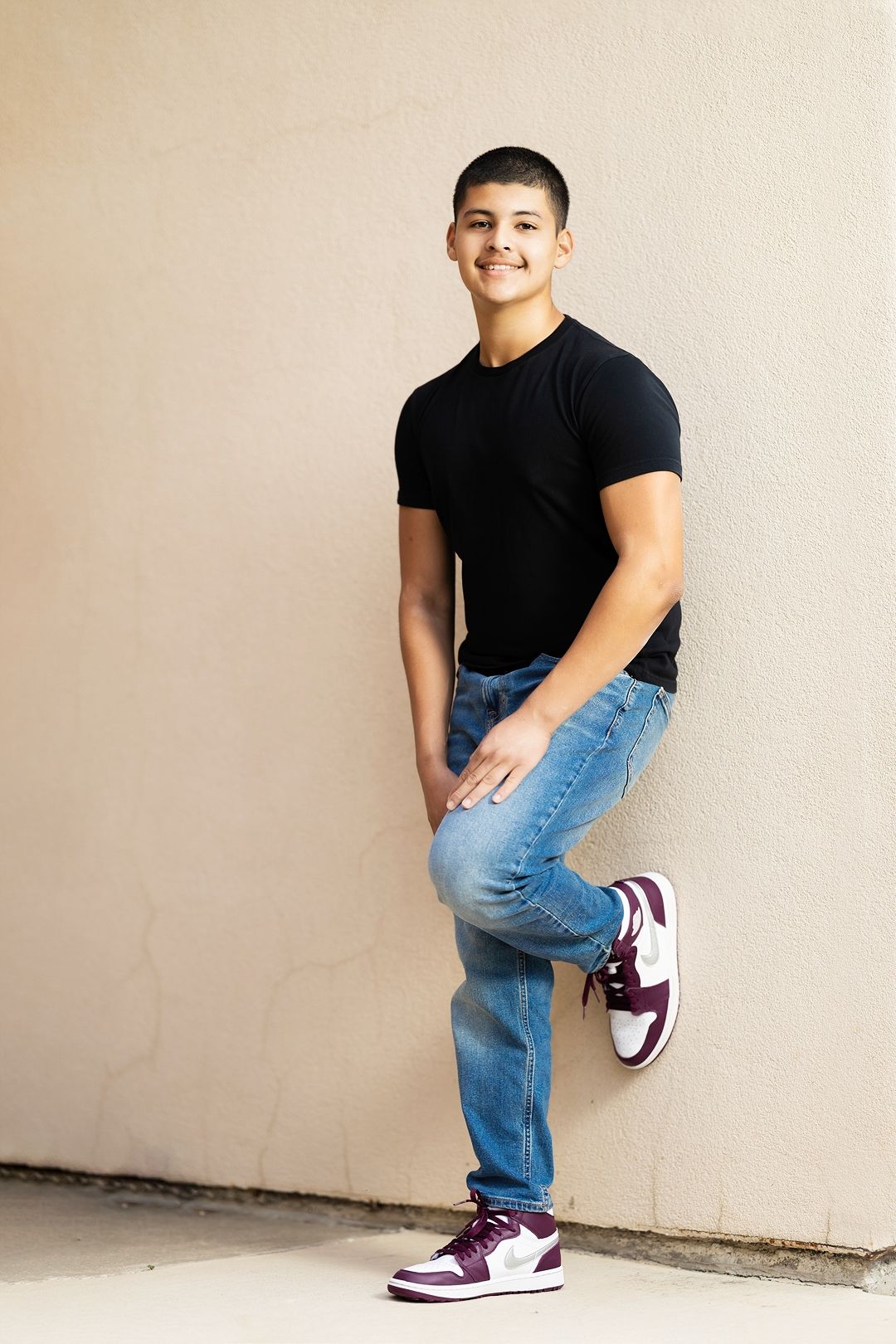 A person in blue jeans and black t-shirt strikes dynamic poses against a beige wall while wearing purple and white sneakers.