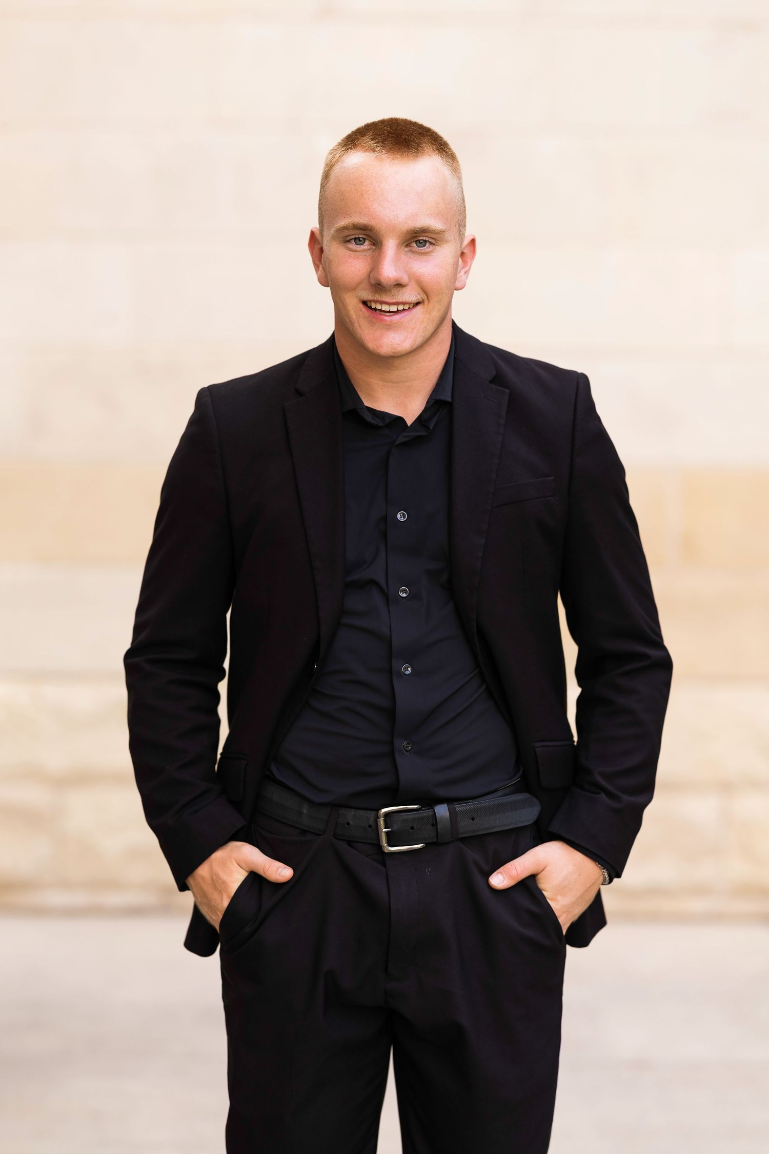 A person wearing a black suit and navy shirt poses against a light background in four similar professional portraits.