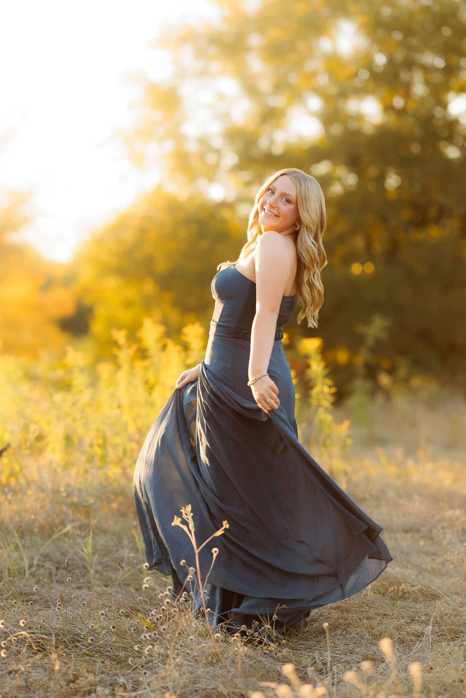 A person in a flowing navy blue dress twirls gracefully in a sunlit meadow during golden hour.
