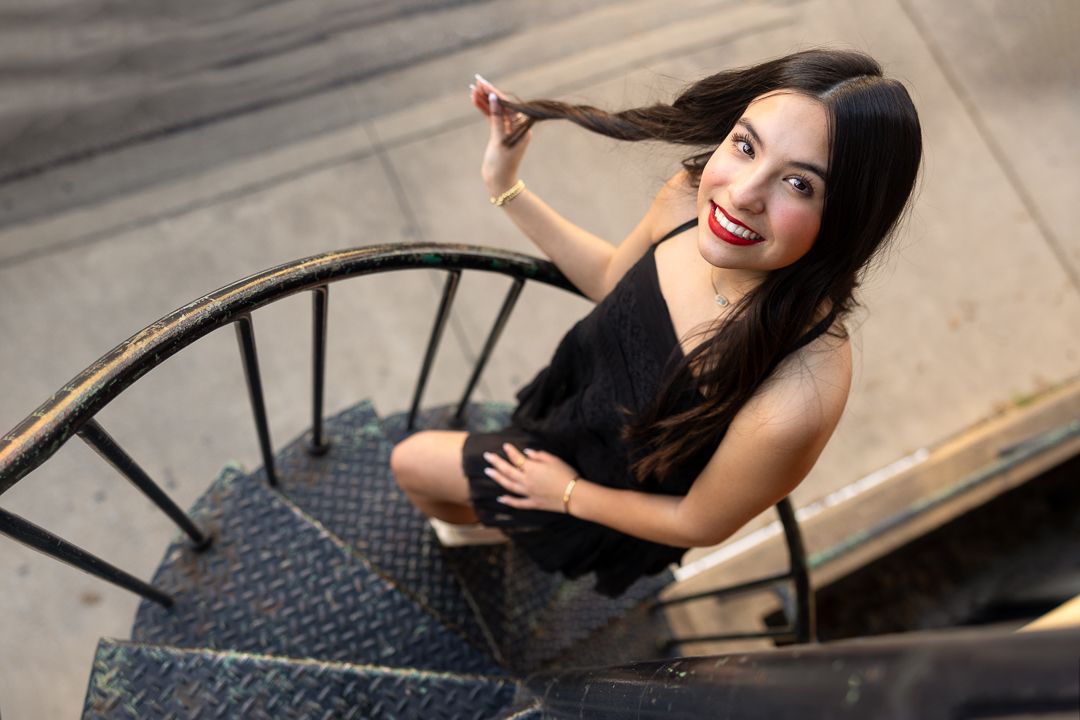 A person in a black dress poses on wooden stairs during a glamour photoshoot session.