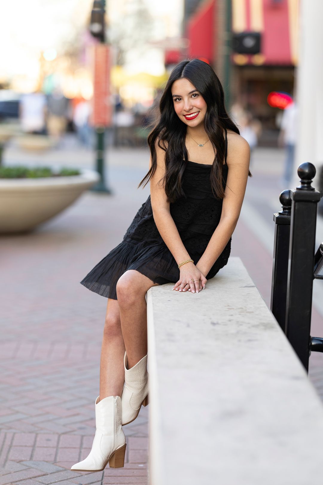 Person in black dress and white boots sits on concrete ledge in urban setting.