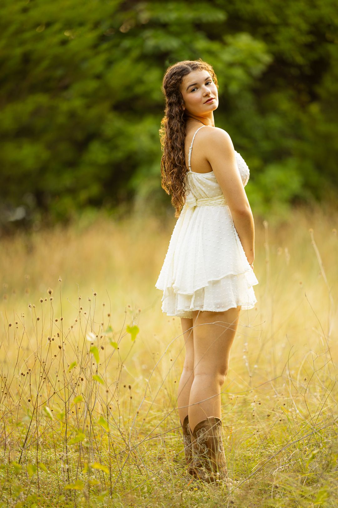 A person in a white dress stands in a golden sunlit meadow during a dreamy summer photoshoot.