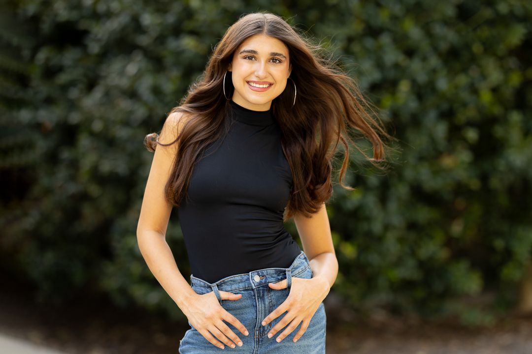 A person in a black turtleneck and blue jeans poses playfully against a dark background.