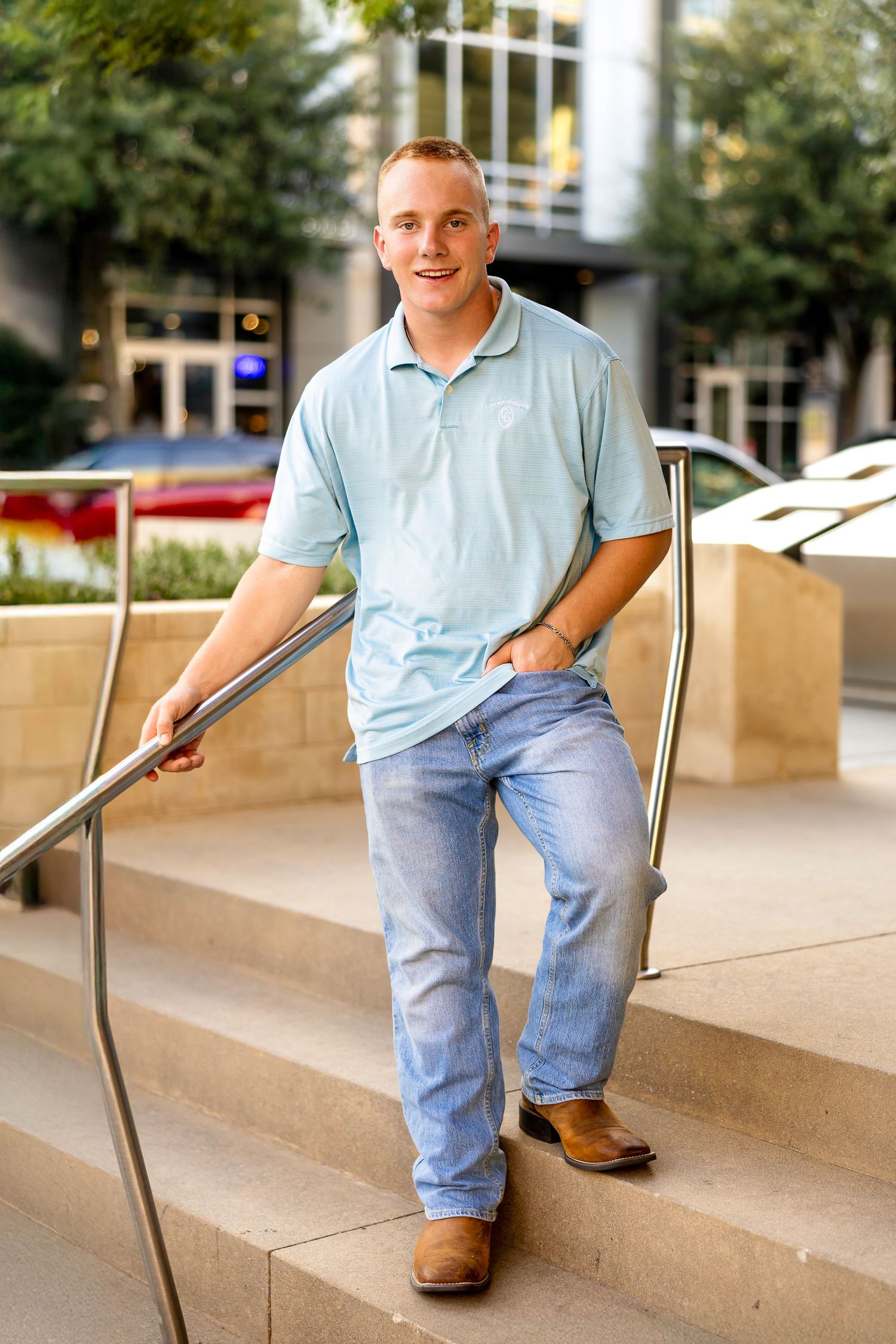 Someone wearing a light blue polo shirt and jeans sits casually on concrete steps in an outdoor urban setting.