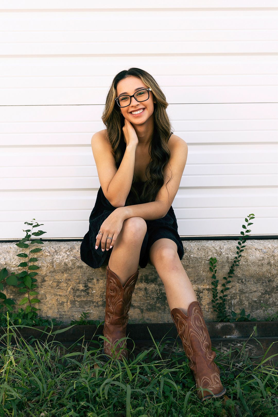 A casual portrait against a white wall featuring brown cowboy boots and a relaxed sitting pose.