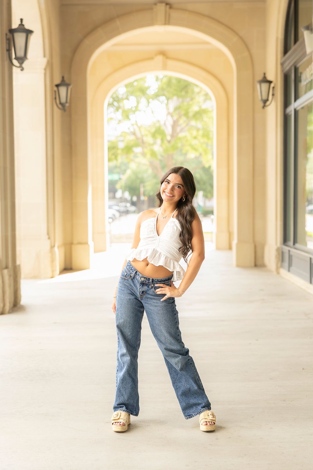 Casual poses in white top and jeans under architectural arches.