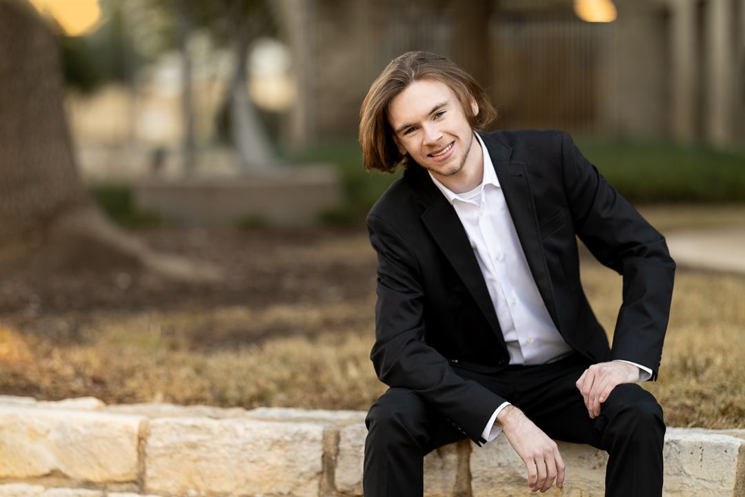 A person in formal attire sits on stone steps outdoors with a warm smile during golden hour.