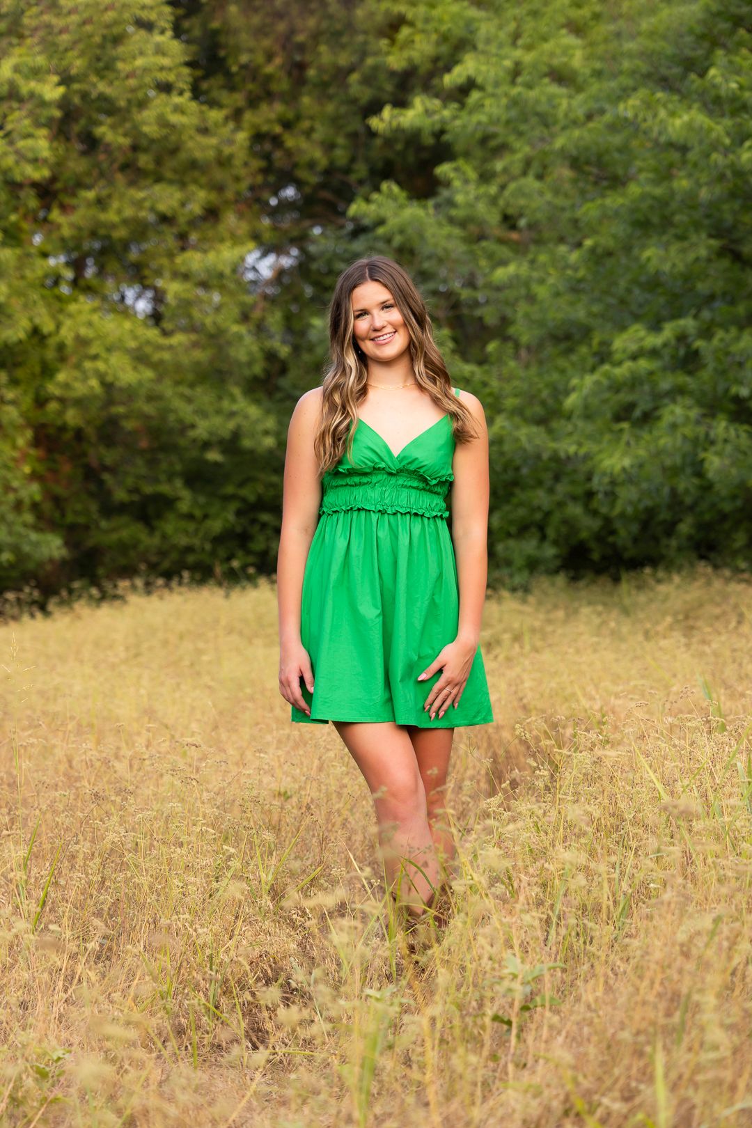 Summer portrait session in bright green dress amid tall grass and trees.