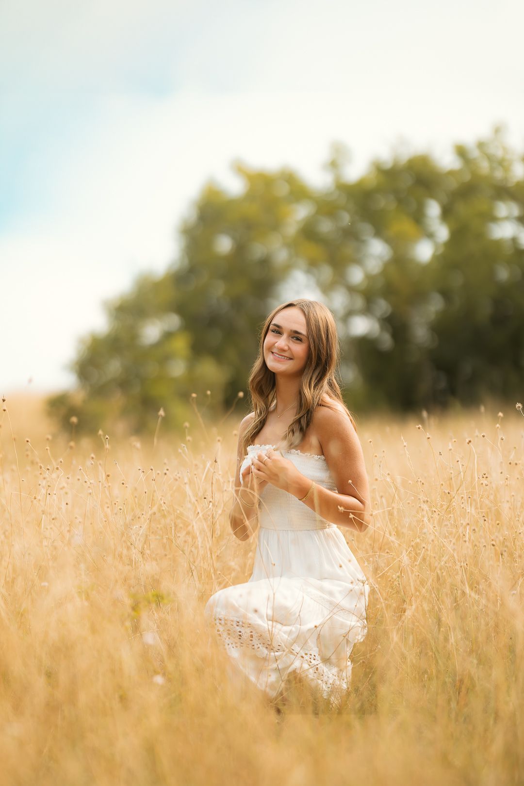 A person in a white dress sits gracefully in a golden wheat field during a summer sunset.