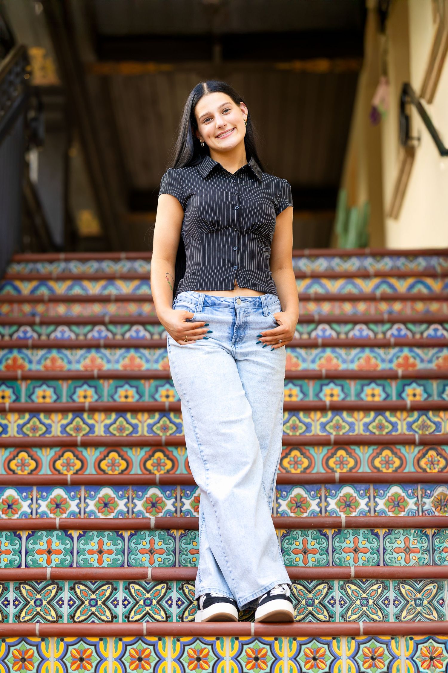Person in black top and jeans sits on decorative tiled steps with turquoise and orange geometric patterns.