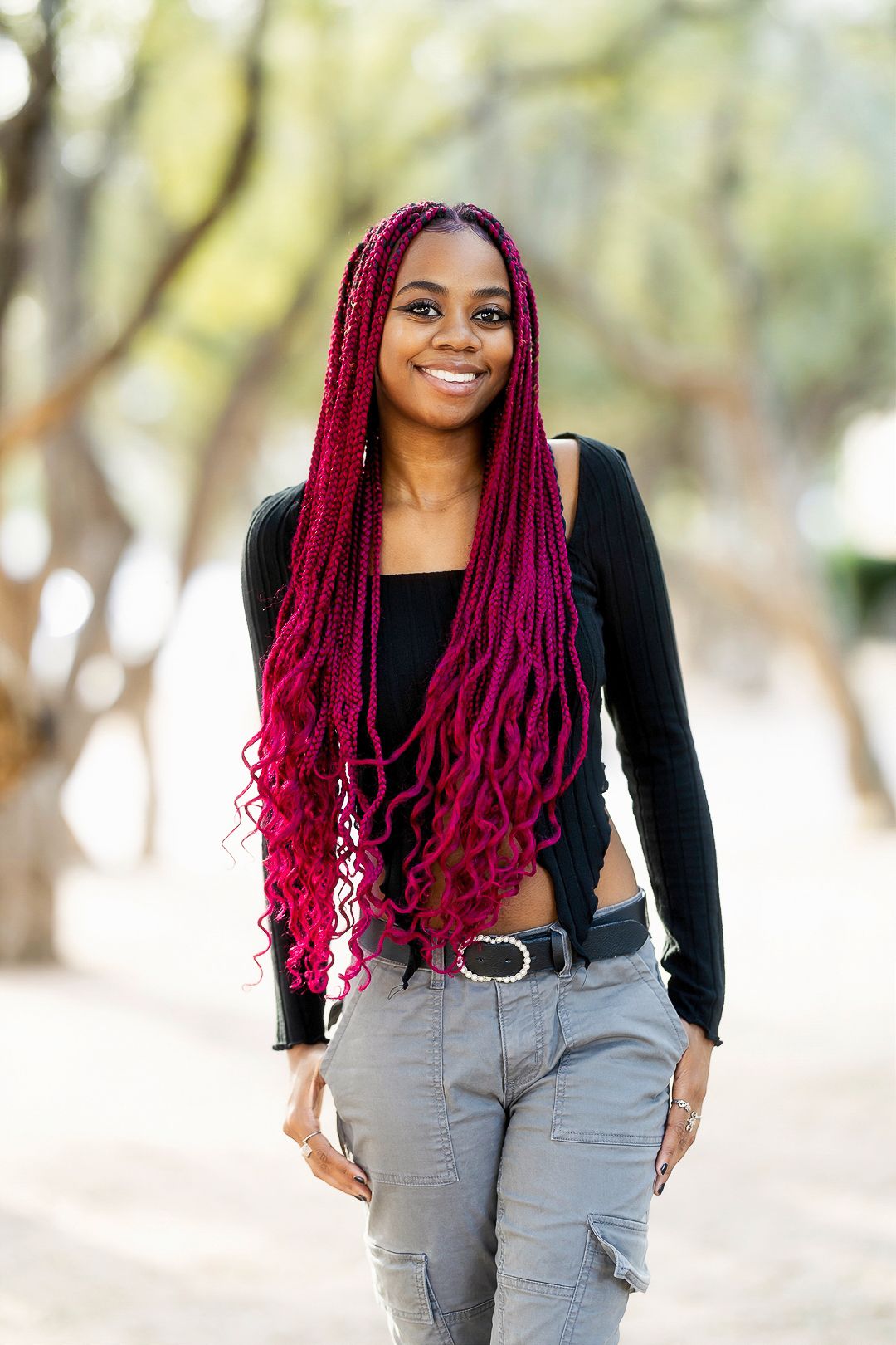 Casual portrait with bright red braids wearing black top and gray pants outdoors.