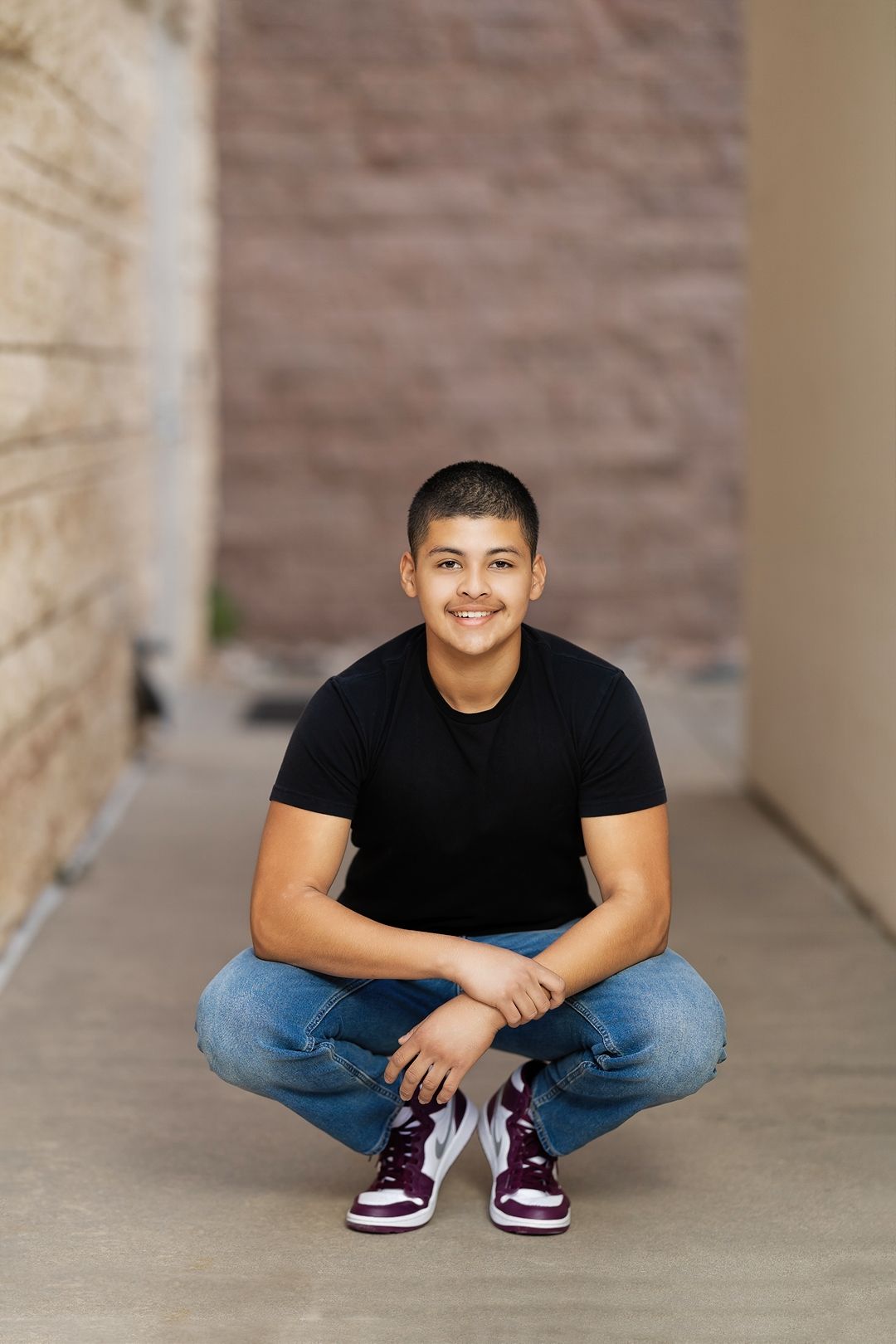 Casual portrait series in jeans and black shirt against textured brick wall background.