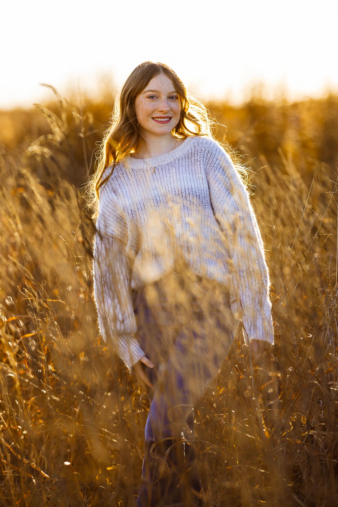 Dreamy golden hour portrait in tall grass wearing a light colored sweater.