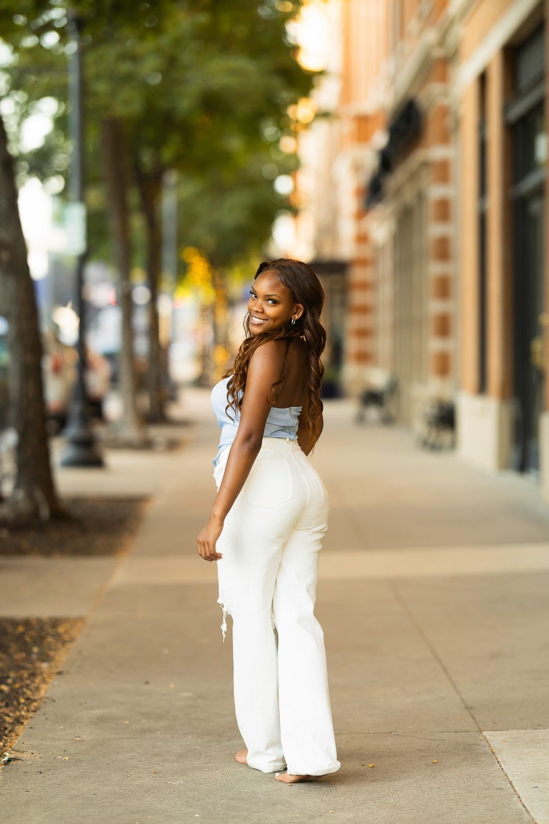 A flowing white jumpsuit ensemble photographed on a city sidewalk with brick buildings.