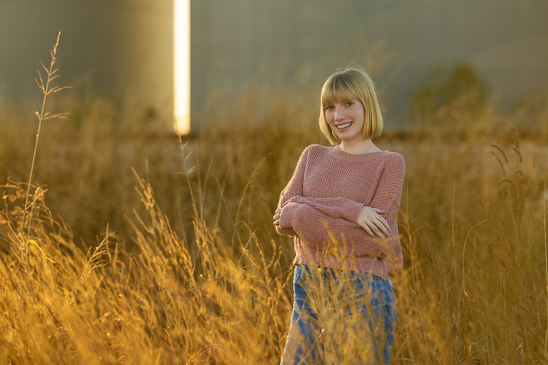 A person in a pink sweater reads a book while sitting in a golden sunlit field during autumn.