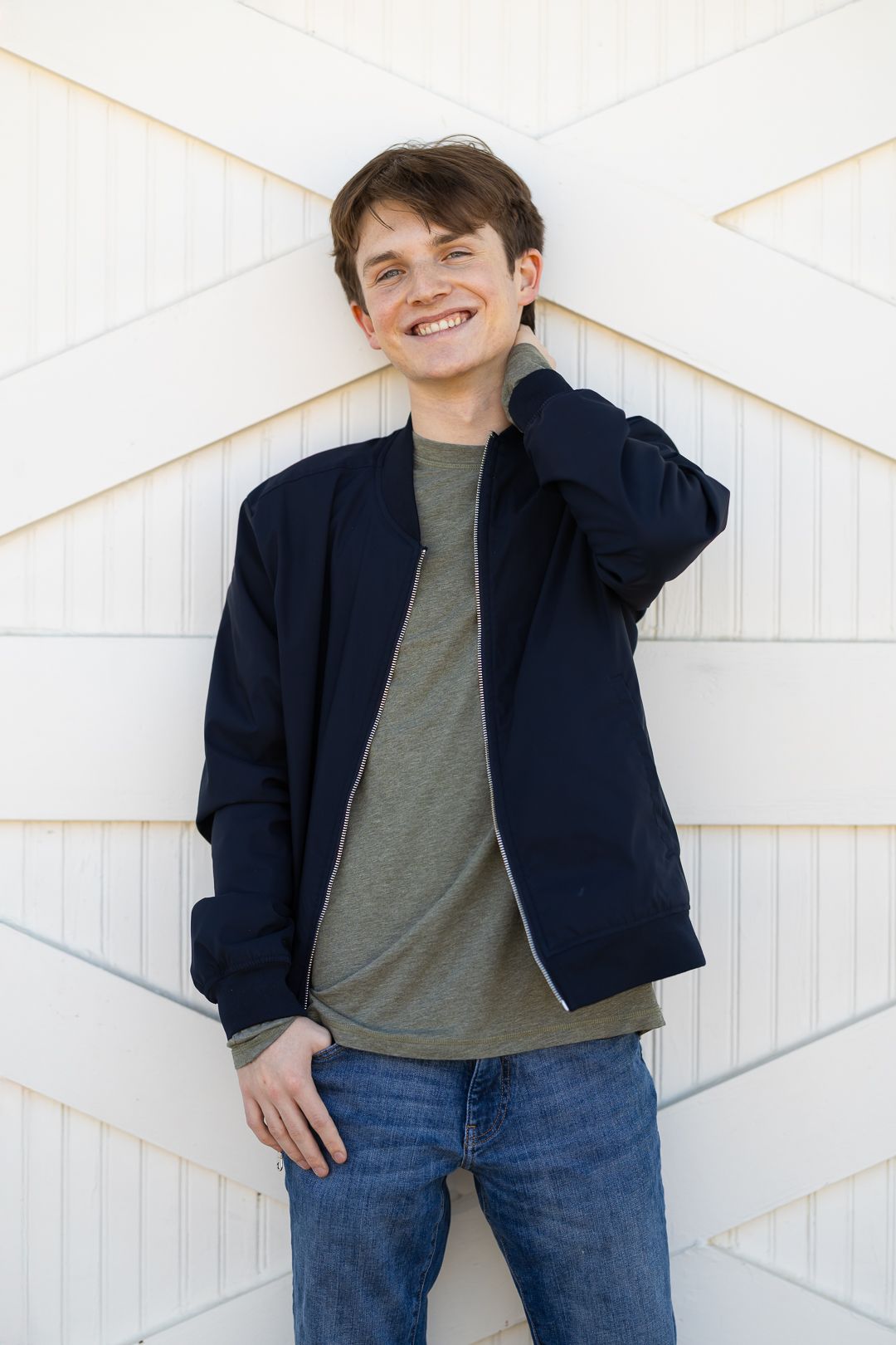 A person wearing a navy jacket and gray t-shirt poses casually against a white diagonal-patterned wall.