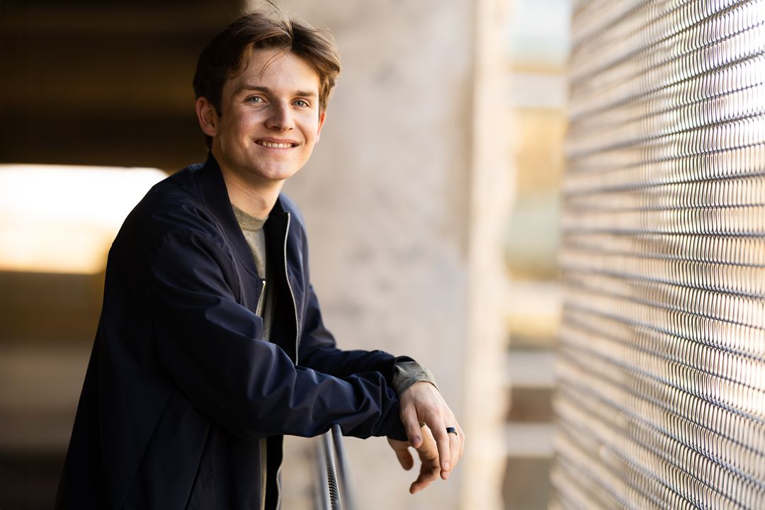A person in a navy blazer poses against a wall with venetian blinds in a series of professional headshots.
