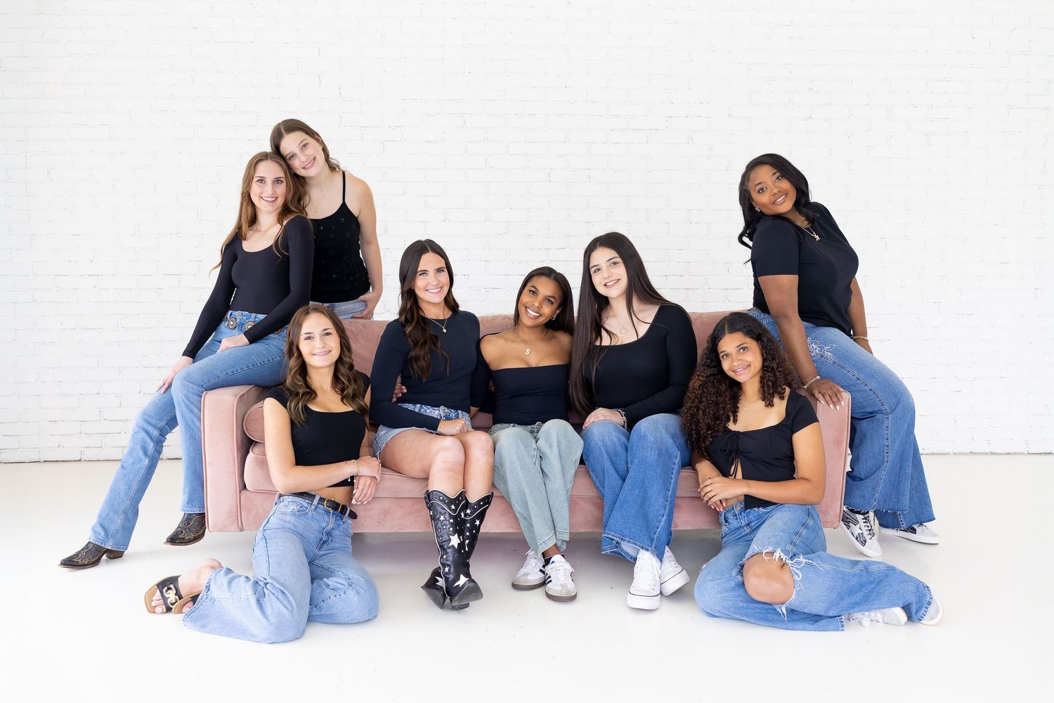 A group of friends in casual denim and black tops sit together against a white wall for a casual photo shoot.