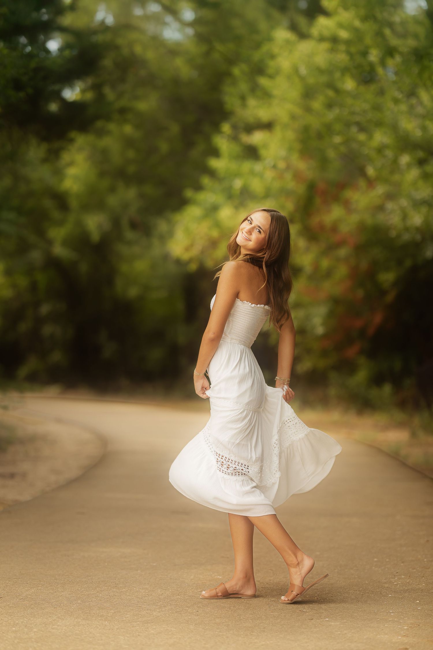 A person in a flowing white sundress twirls barefoot on a sunlit garden path surrounded by lush greenery.