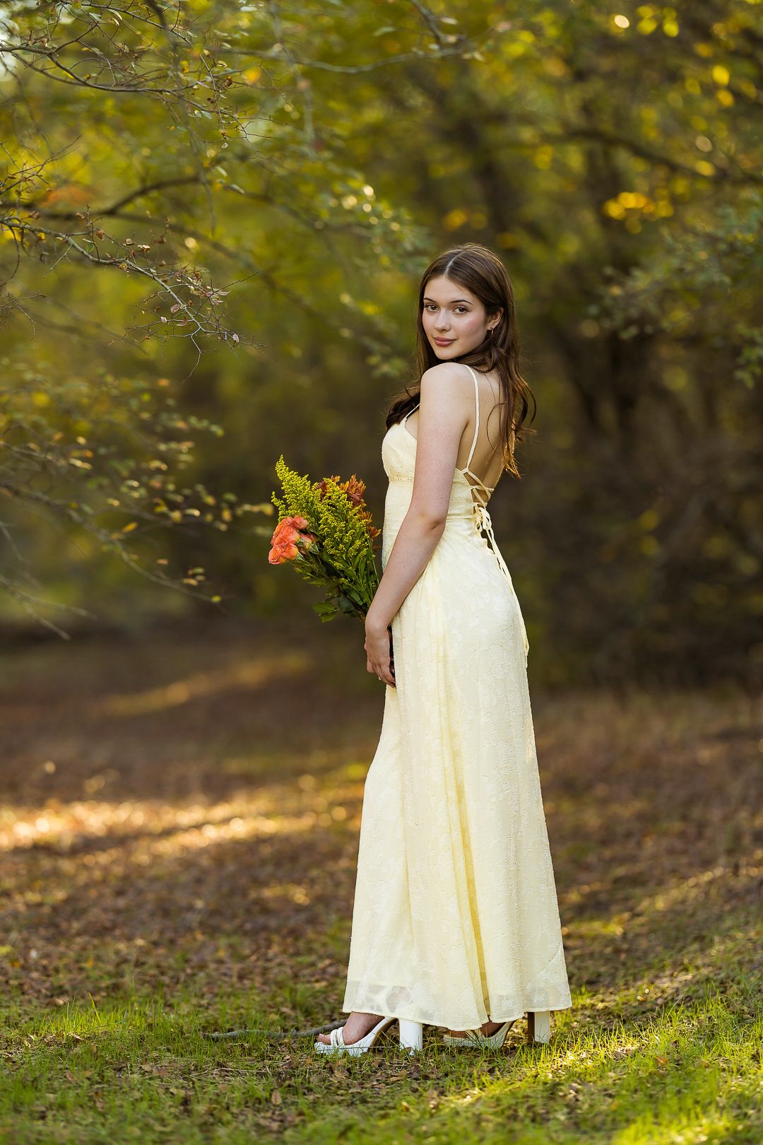 Elegant yellow dress photoshoot on a grassy hillside with autumn trees.