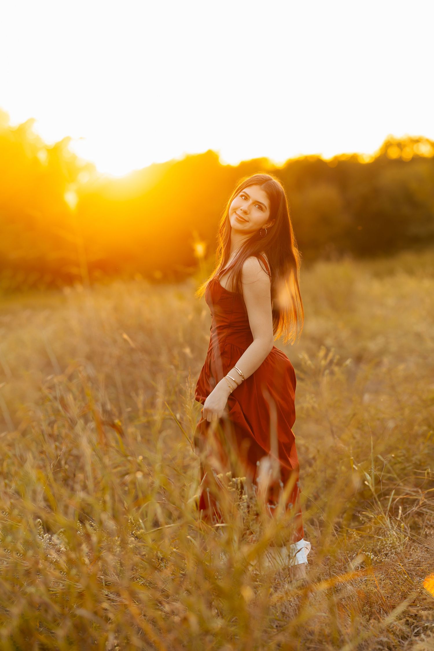 A person in a red dress stands in a golden field at sunset with warm glowing light creating a dreamy atmosphere.